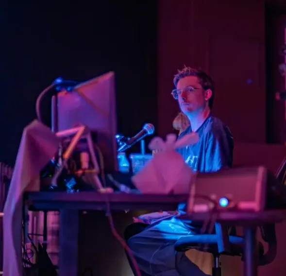 Brayden Young programming a lighting console in a rehearsal room lit in blue and magenta